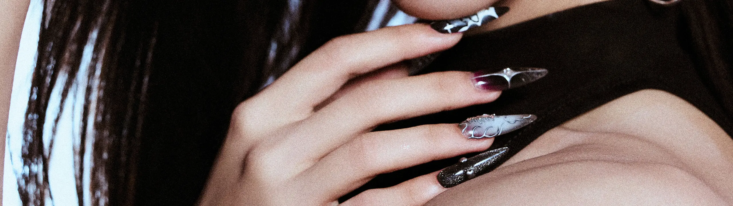 Close-up of a model’s hand wearing long sculpted press-on nails with metallic 3D textures and dark gothic gradients.
