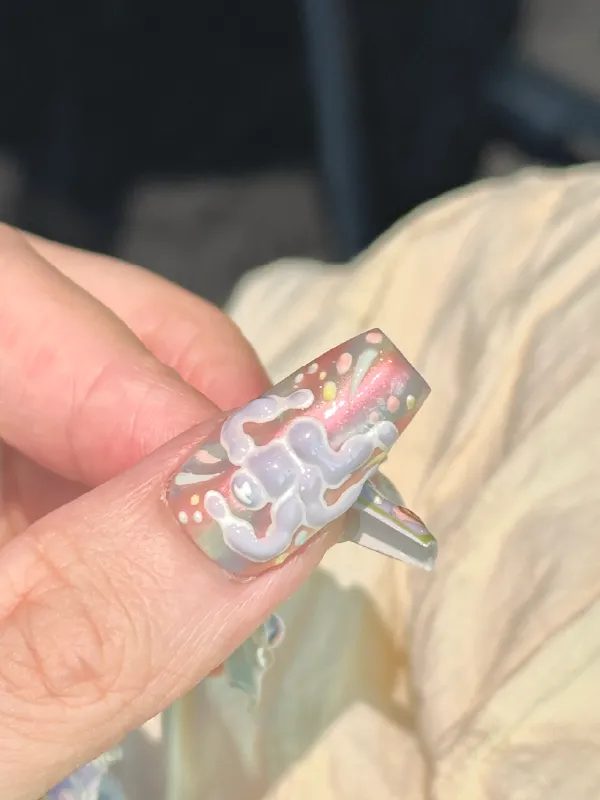 A close-up of a hand wearing silver textured abstract press-on nails.
