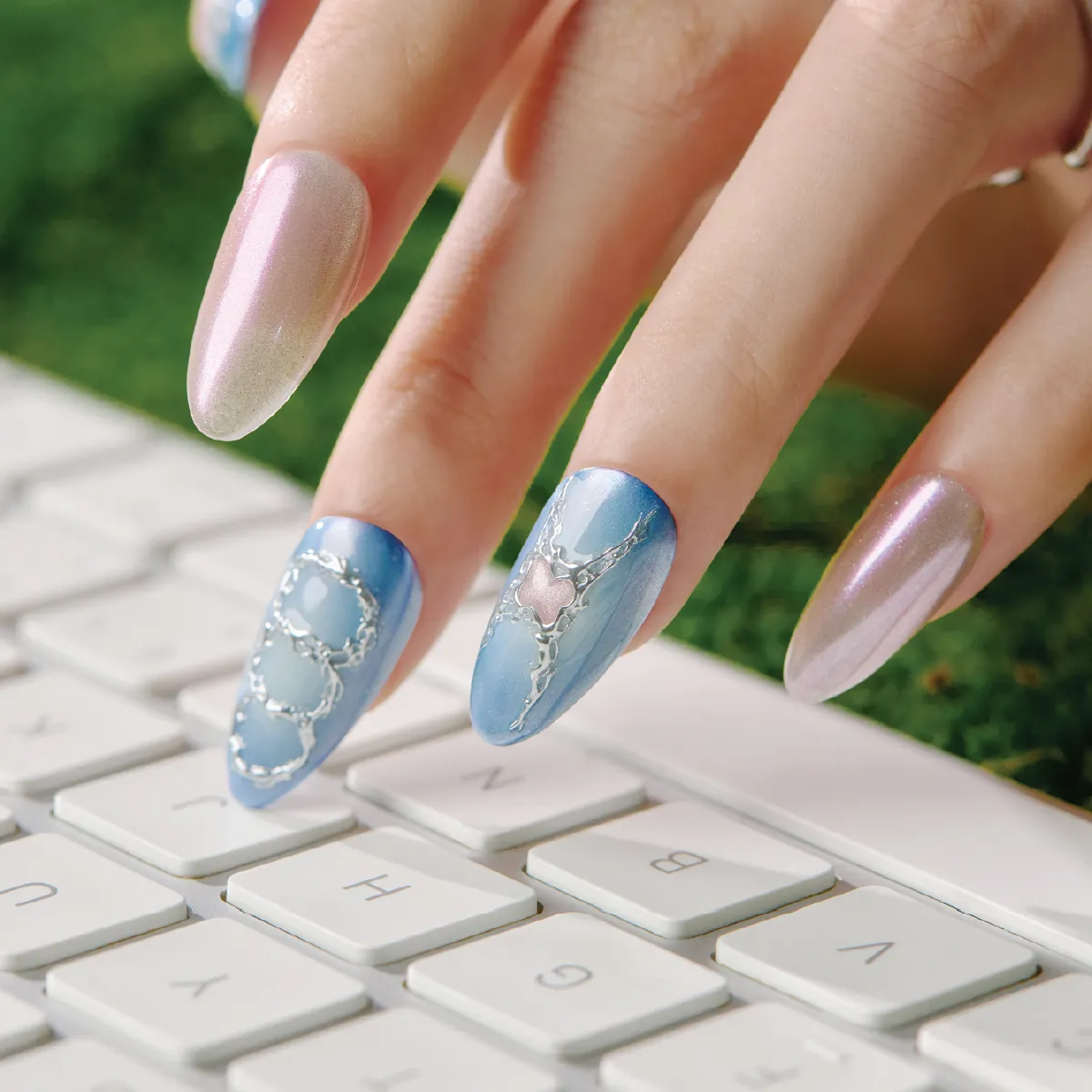 Close-up of blue candy medium almond press-on nails with silver outline details on keyboard.