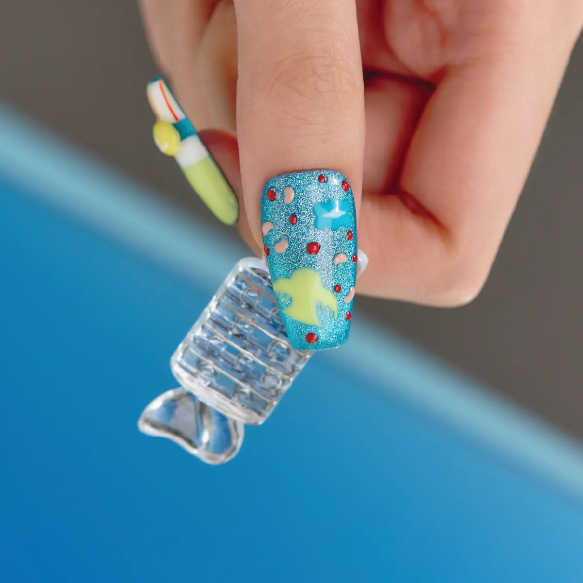 Close-up of Candy Night blue glitter long coffin press-on nail with abstract pastel shapes and red dot accents.