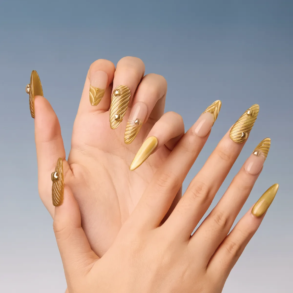 Close-up of long almond gold textured press-on nails with nude base accents and 3D gold embellishments.