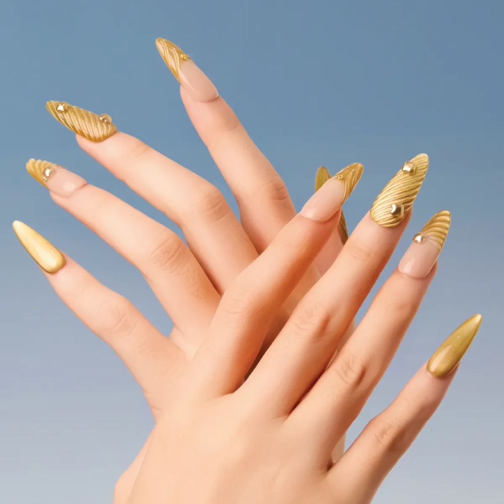 Model hands displaying gold ribbed long almond press-on nails styled with nude negative space.