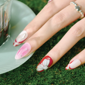 Cherry Stardust press-on nails displayed beside a glass teacup, showing red contour tips and pink stardust nail art