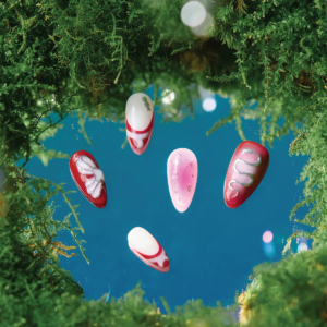 Five-piece Cherry Stardust press-on nail set floating above a mirror surrounded by green moss