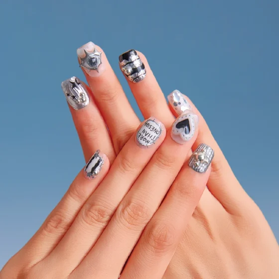 Close-up of both hands wearing Chrome Vision short square nails featuring black-silver patterns, text details, heart design, and metallic studs.