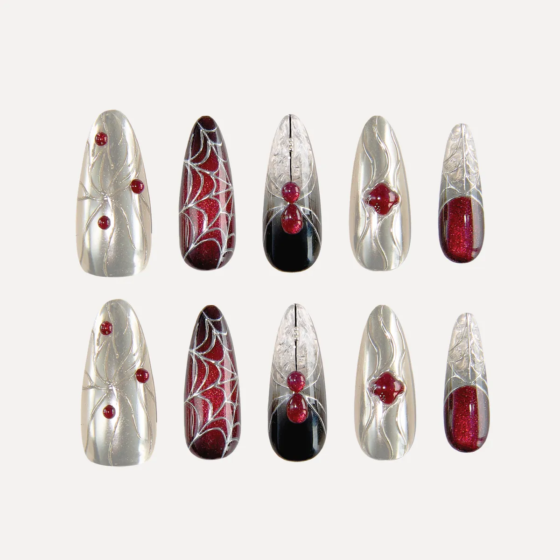 Flat-lay display of the “Crimson Whisper” long oval press-on nail set featuring silver chrome textures, red gem accents, and black-red gradient spiderweb designs.