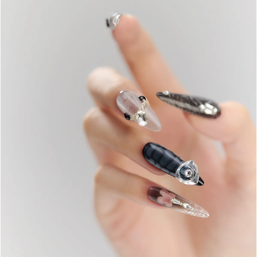 Close-up of Cyber Pulse long stiletto nails with crystal embellishments, metallic textures, and futuristic black-and-silver patterns