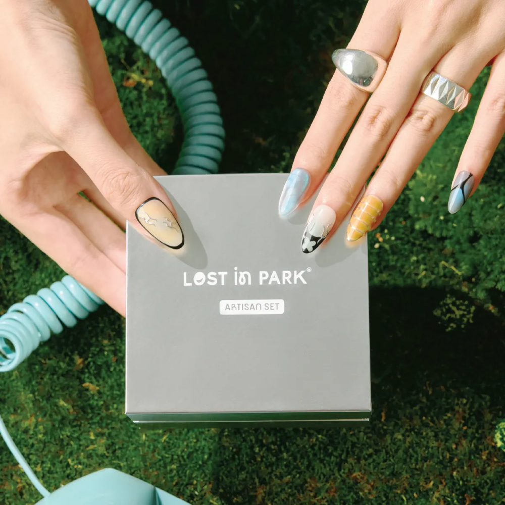 Hands wearing Deconstruct Vision press-on nails holding a LOST in PARK Artisan Set box, showcasing geometric and abstract nail designs