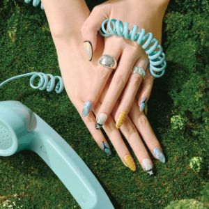 Full hand view of Deconstruct Vision press-on nails featuring abstract patterns, grid textures, and glossy blue accents against a moss background