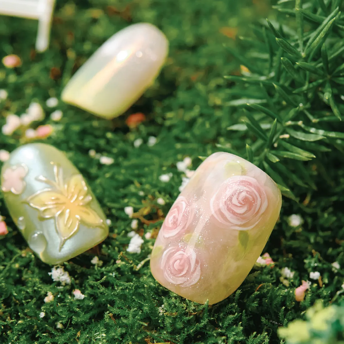 Close-up of Dewy Garden press-on nails with hand-painted pink roses, butterfly embossing, and dewy droplet effects on green grass