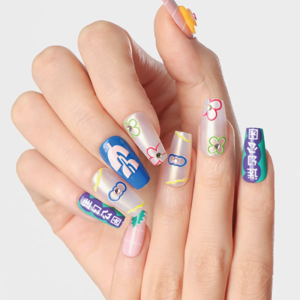 Hand pose displaying mixed flower, graphic, and pastel grid press-on nail designs