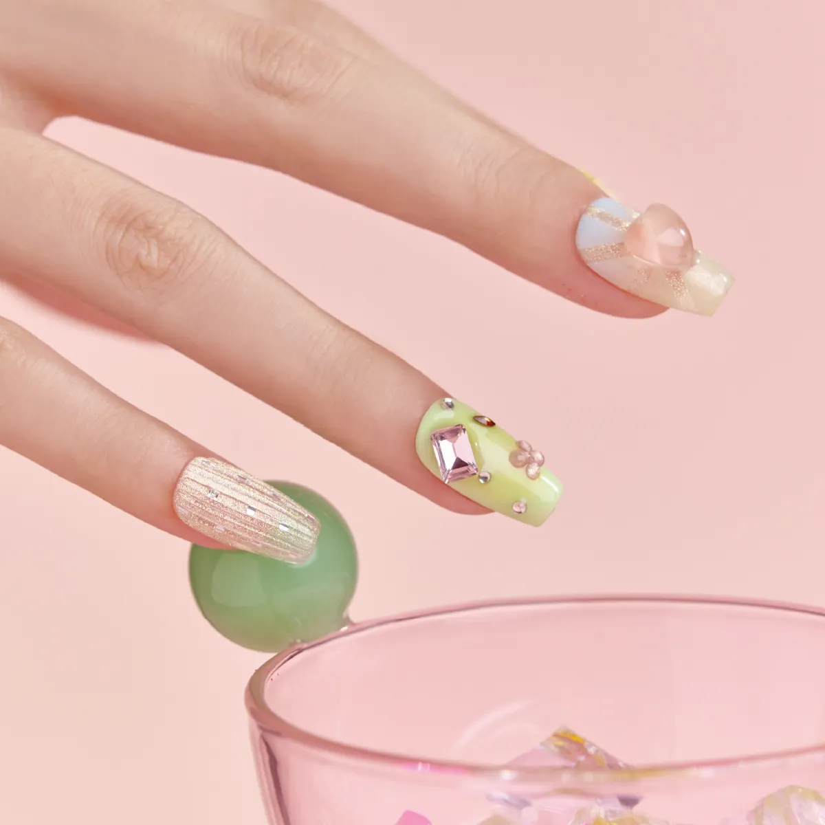 Close-up of pastel green and pink gemstone press-on nails with textured glitter accent