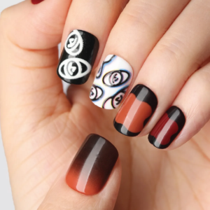 Close-up of press-on nails in deep red and black tones with abstract white eye illustrations and gradient effects on fingers.