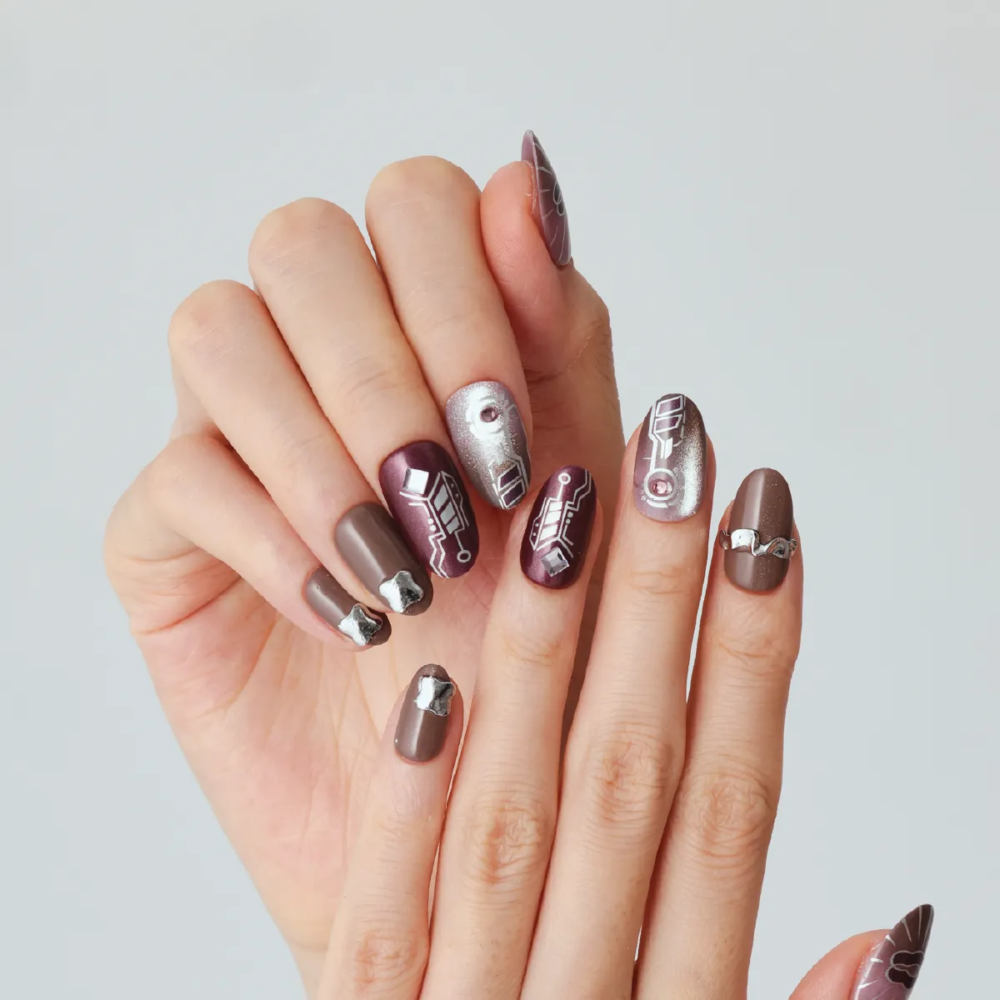 Hand with futuristic silver and plum press-on nails featuring circuit-inspired patterns and 3D embellishments