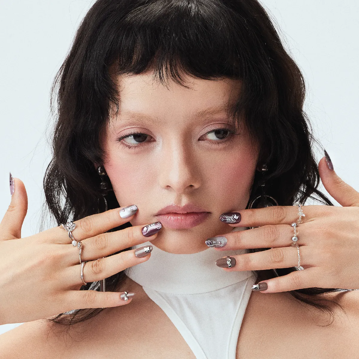 Model holding hands up to face with glam cyber-inspired press-on nails and silver rings
