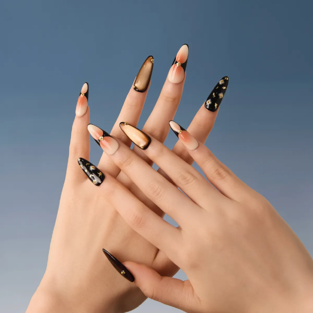 Artistic hand pose showcasing long almond press-on nails in a mix of translucent brown and black designs with embellishments.