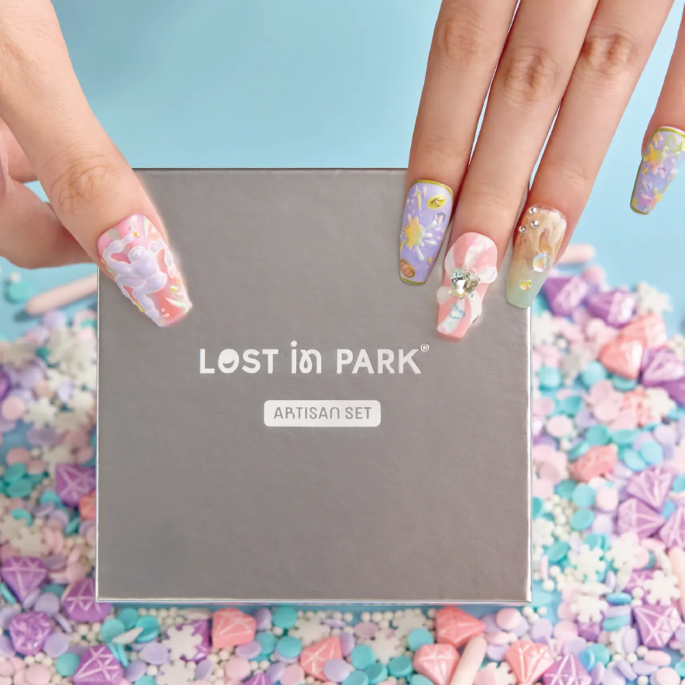 Hand with pastel press-on nails holding LOST in PARK silver box, surrounded by candy-like nail props.