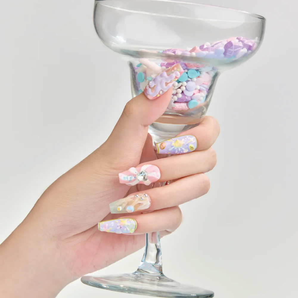 Close-up of pastel 3D press-on nails holding a cocktail glass filled with confetti.