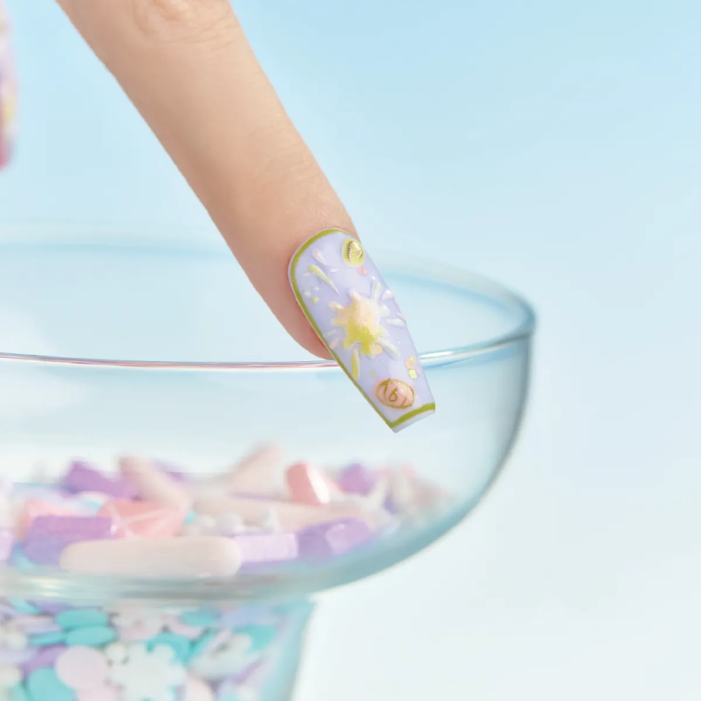 Lavender and gold star design nail resting on rim of glass bowl filled with pastel nail pieces.