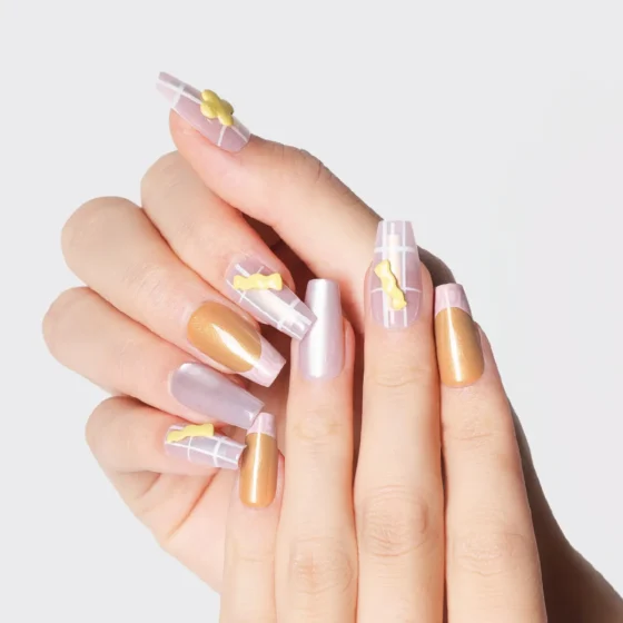Close-up of long almond press-on nails with gold shimmer and pink grid design, decorated with 3D yellow candy charms