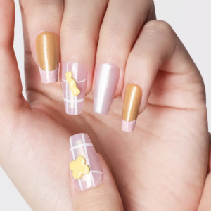 Detailed close-up of pink grid press-on nails with yellow flower-shaped 3D charm and gold accent nails.