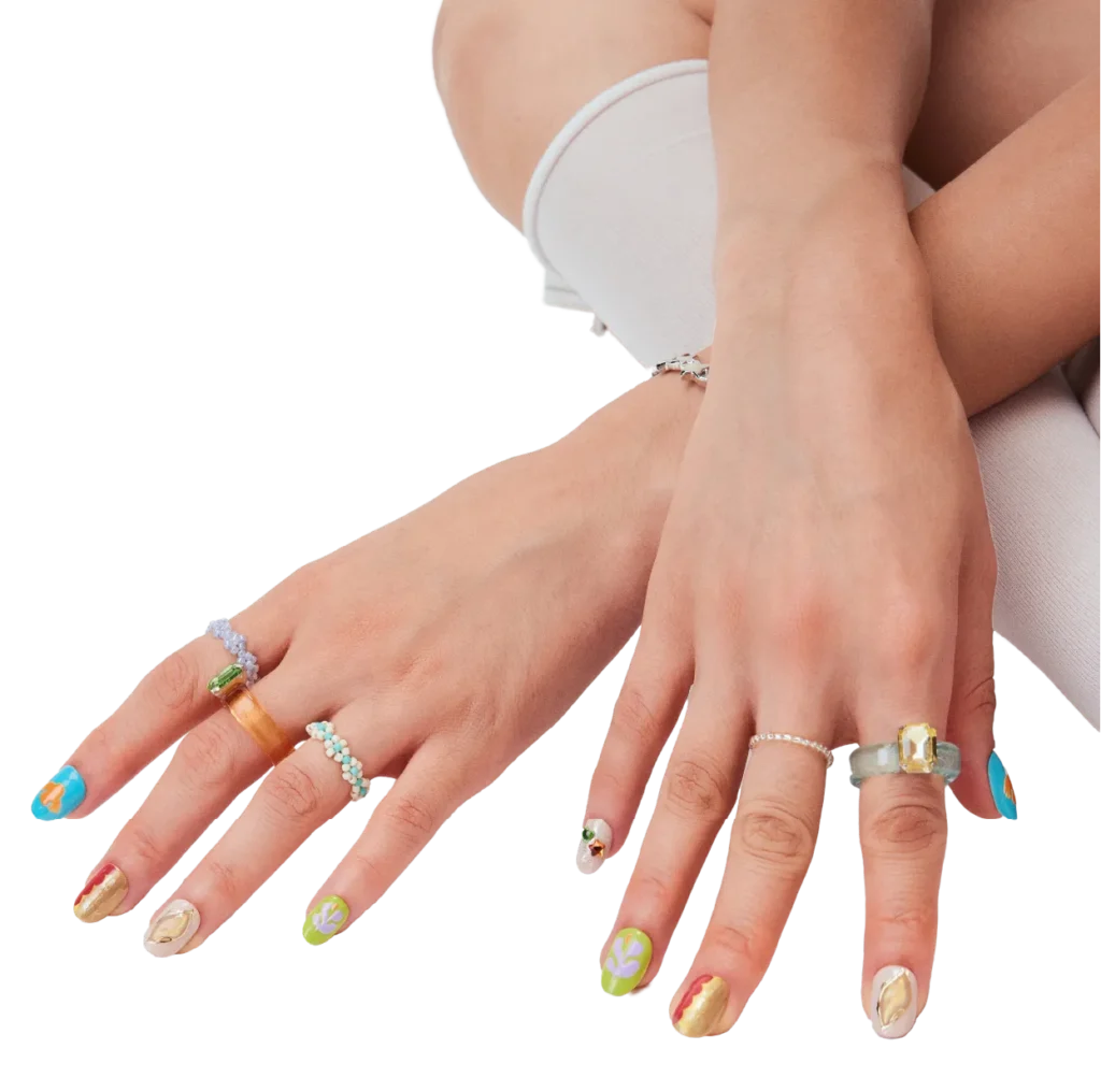Model’s hands wearing colorful mixed-design press-on nails by LOST in PARK, with layered rings and a soft minimal background.