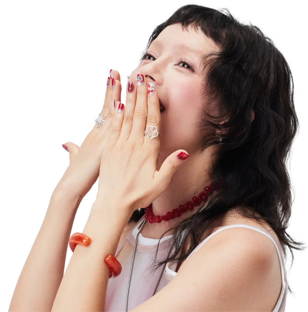 Smiling model with red press-on nails covering her mouth, wearing playful jewelry, LOST in PARK