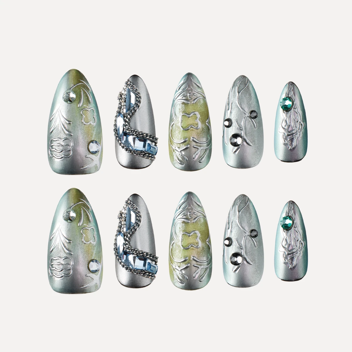 Medium almond press on nails flat lay in silver green tones with embossed patterns chains and gemstone details